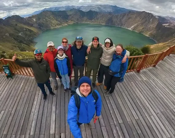 Eine Gruppe von Wanderern posiert auf dem hölzernen Aussichtspunkt Shalala mit Blick auf den türkisfarbenen Kratersee Quilotoa während der Quilotoa-Rundwanderung in Ecuador.