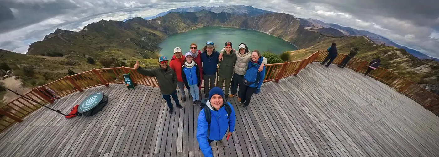 Eine Gruppe von Wanderern posiert auf dem hölzernen Aussichtspunkt Shalala mit Blick auf den türkisfarbenen Kratersee Quilotoa während der Quilotoa-Rundwanderung in Ecuador.