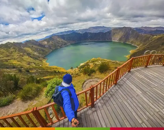 Ein Wanderer in einer blauen Jacke blickt während der Quilotoa-Loop-Wanderung in Ecuador vom hölzernen Aussichtspunkt Shalala auf den Kratersee von Quilotoa.
